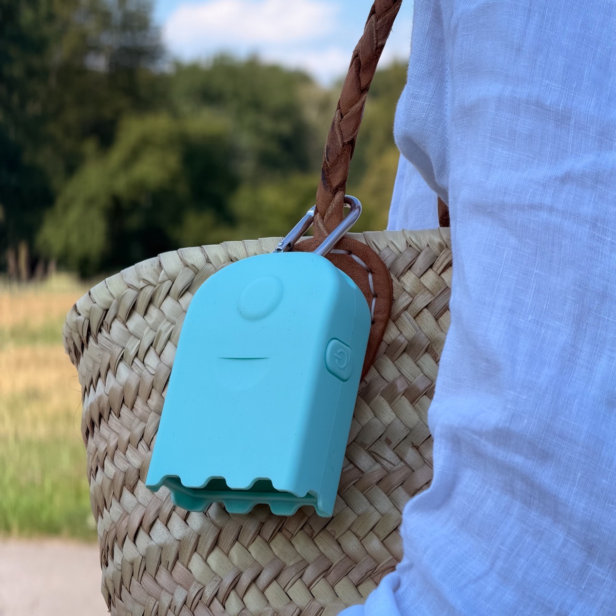 A teal AirBeam Mini clipped by a carabiner to a woven straw tote bag outdoors